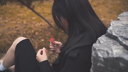 女生倚石惆怅掰花瓣情绪背影视频的预览图