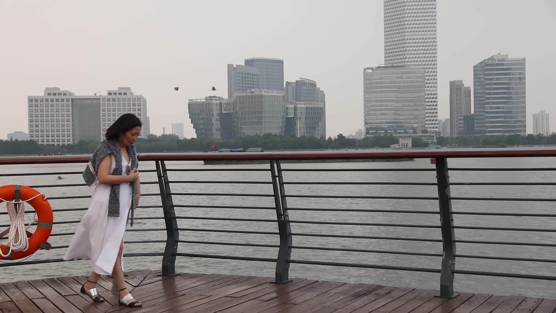 走在城市江边看都市风景思考的女人侧面视频的预览图