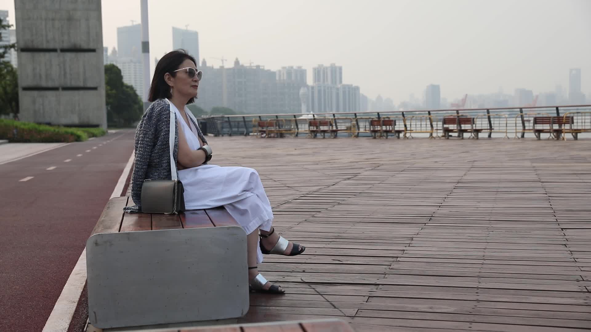 坐在城市江边看都市风景思考的女人侧面视频的预览图