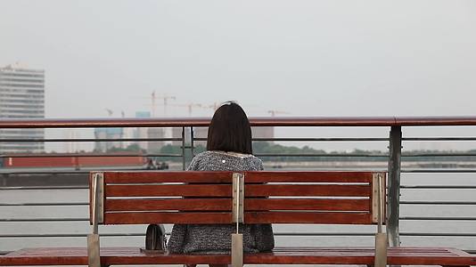 坐在城市江边看都市风景思考的女人背影视频的预览图