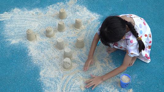 在蓝色地面上玩沙子的小女孩视频的预览图