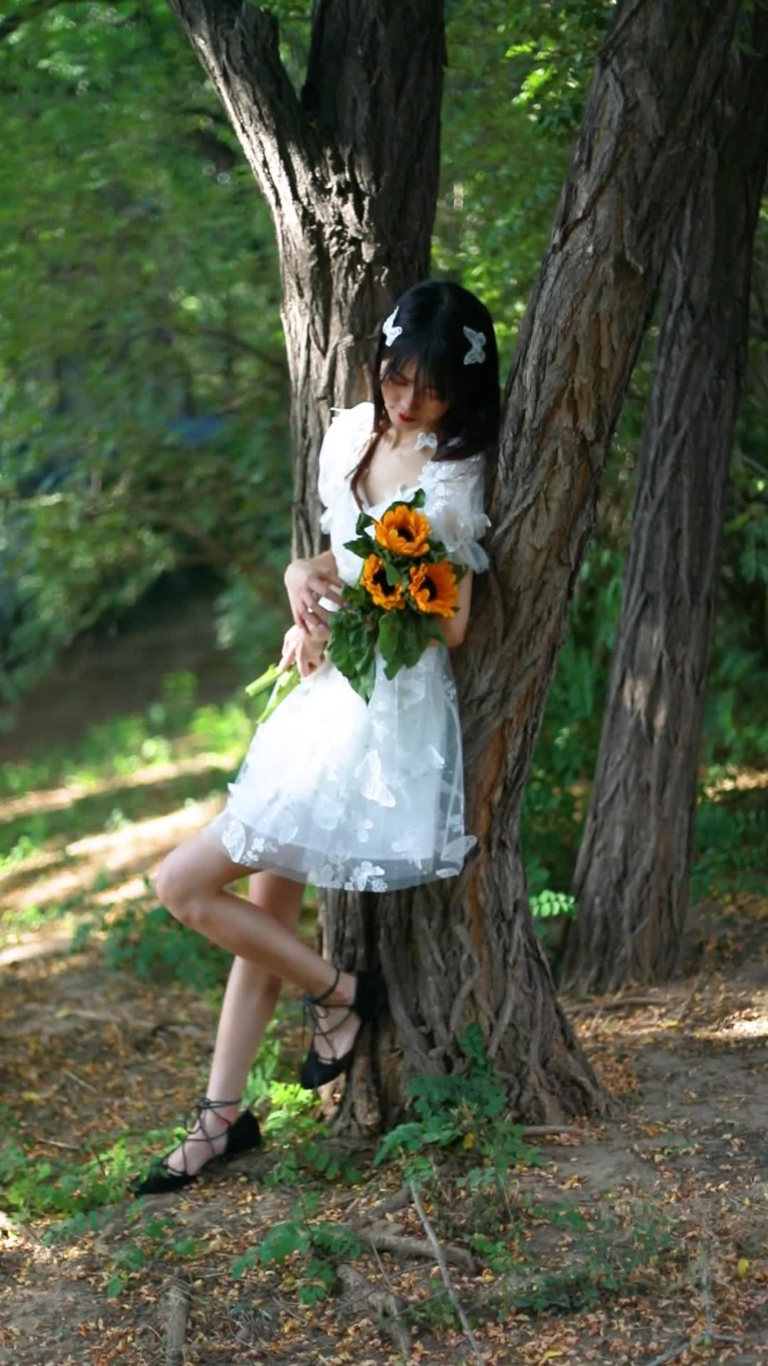 穿着白色连衣裙的女孩拿着花在树林里写真拍摄视频的预览图