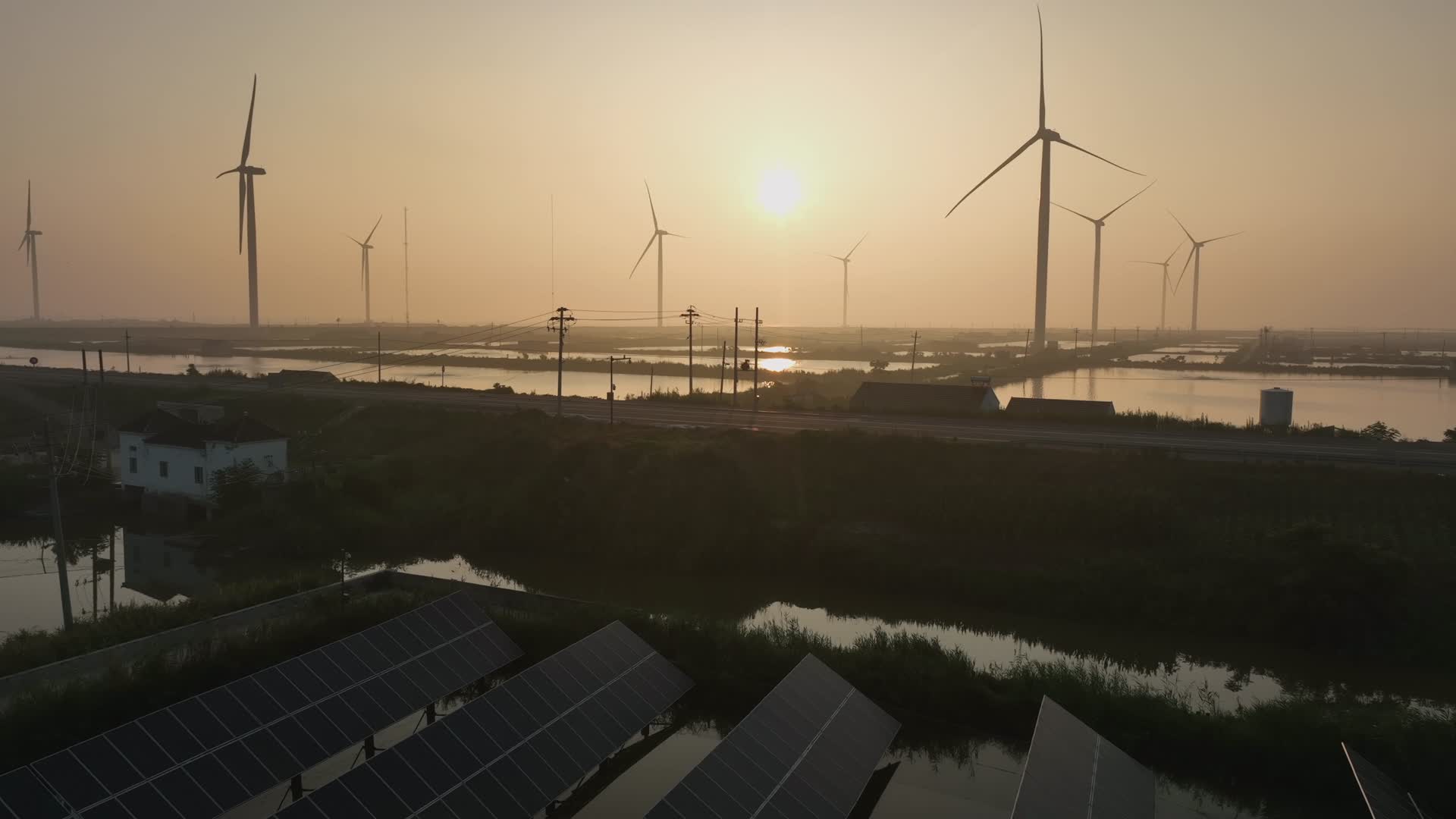 日出下的乡村里的太阳能光伏板和风力发电机视频的预览图