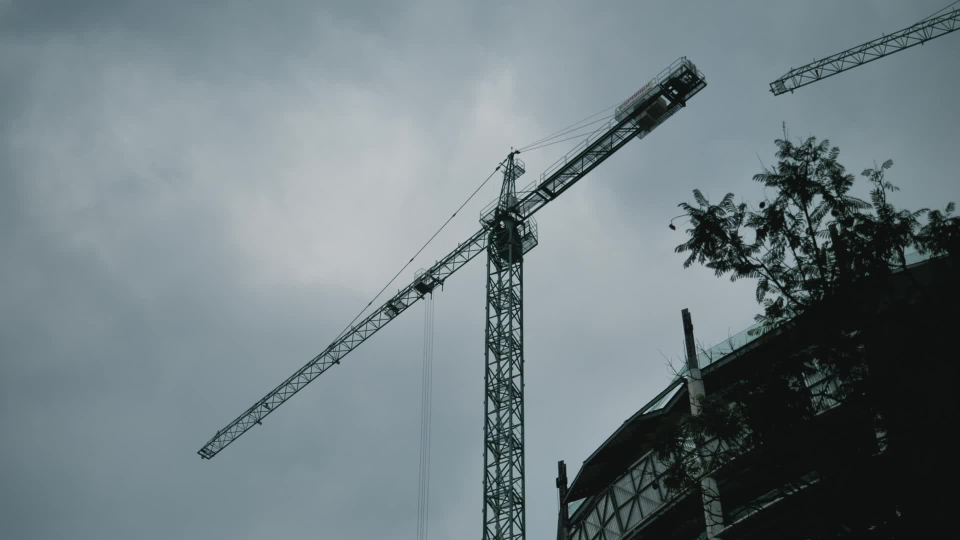 一架飞机从建筑施工的塔吊上空飞过天气阴沉视频的预览图