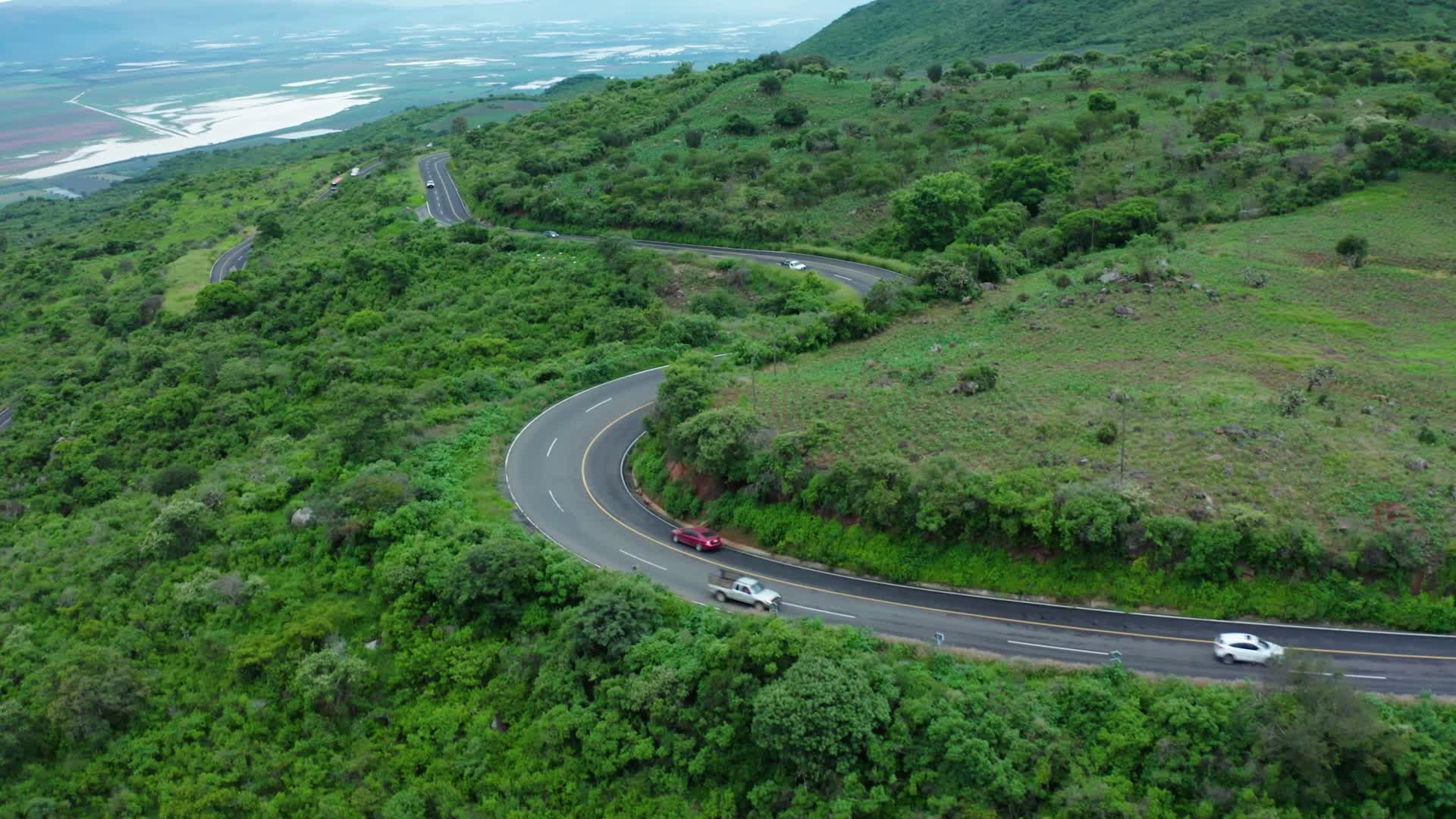 航拍平原丘陵绿水青山中里蜿蜒盘旋的公路视频的预览图