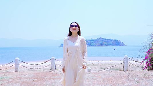 身穿白色裙子戴着墨镜在海边沙滩散步的美女视频的预览图
