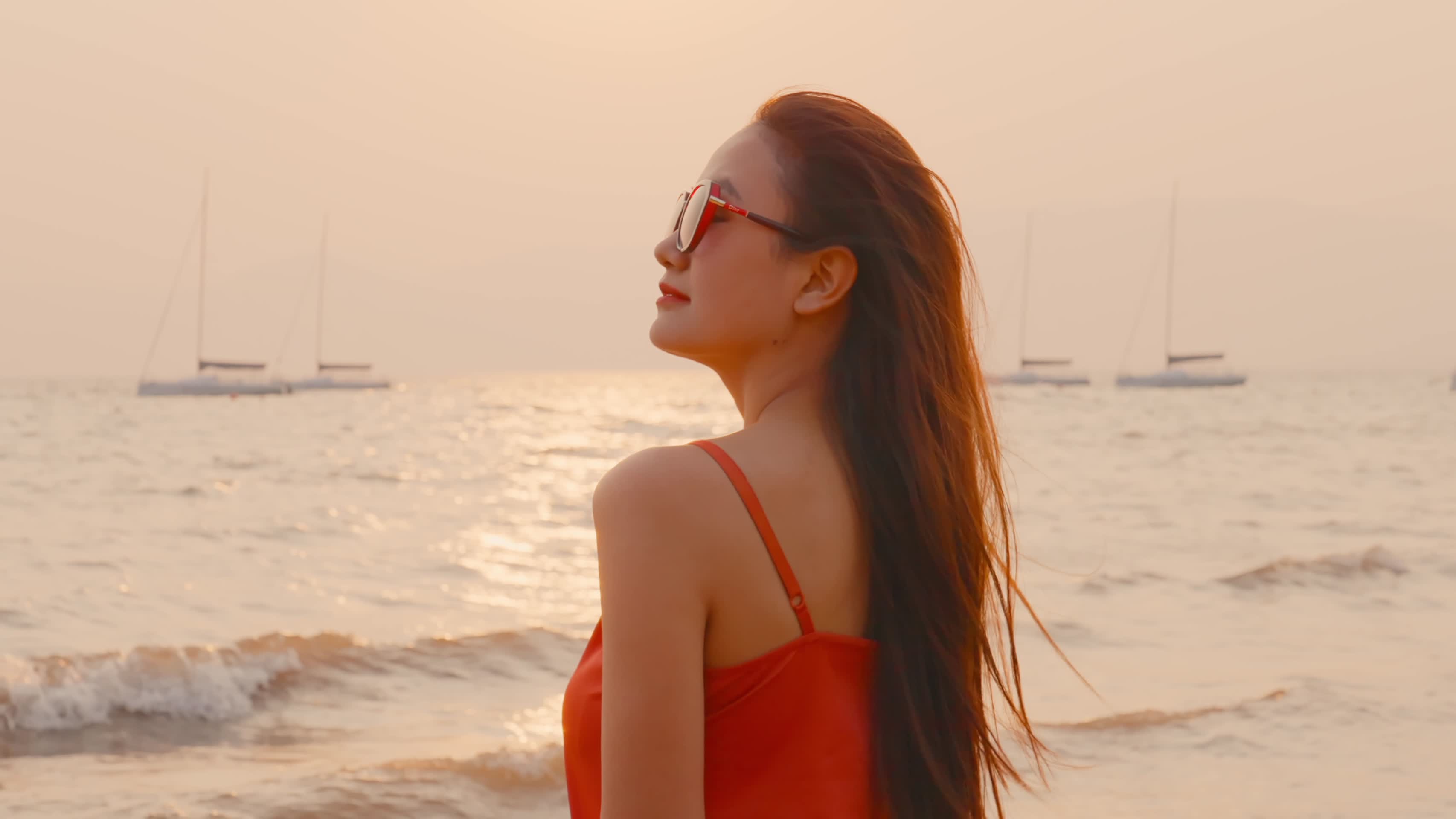夕阳晚霞间海边身穿红裙戴着墨镜的美女视频的预览图