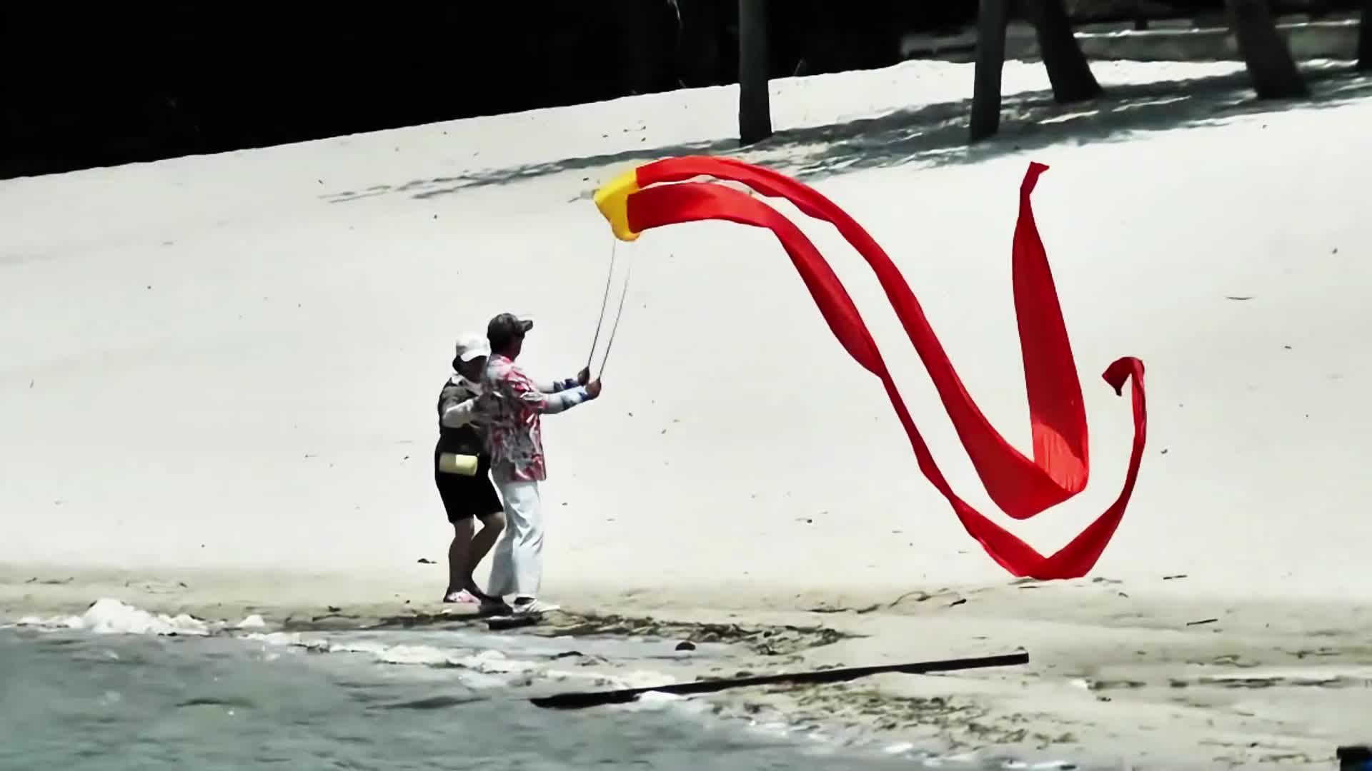 沙滩上手舞红飘带的人视频的预览图